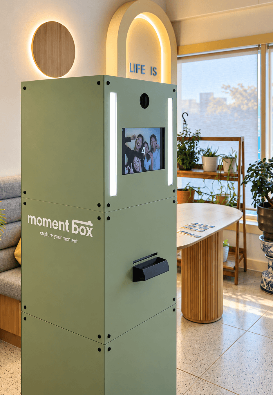 Green Moment Box photo booth inside CAFE NUL, with guests on the capture screen and printed photos on the adjacent table